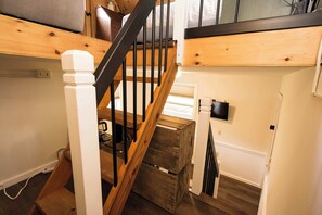 A staircase with wooden steps and black railings, leading to a lofted area with a bed and a television mounted on the wall. - Lakefront Tiny House w/ Free Tix | Dock + Dogs OK (Lake Lure)