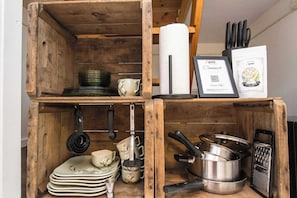 Un meuble de rangement en bois, doté d’étagères où sont rangés des ustensiles de cuisine, une râpe et un certificat encadré.