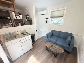 Une cuisine compacte équipée d’une cuisinière, d’un évier et de meubles blancs. Un canapé bleu et une petite table en bois se trouvent dans l’espace salon.