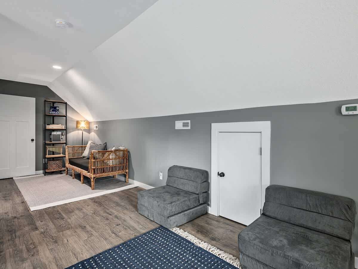 Een ruime kamer met een grijze bank, een rieten stoel en een boekenkast.