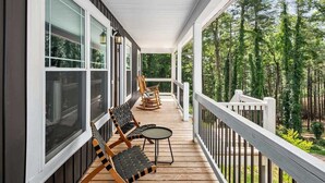A covered porch with wooden flooring, white railings, and two rocking chairs.