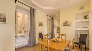 A dining area with a wooden table and chairs, a bowl of fruit, and a window with curtains. - Lovely 4 bedrooms apartment 30m SanGiovanni metro (Roma)