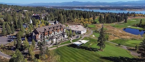 Un complejo de cabañas con varios edificios, campo de golf y un lago al fondo.