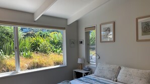 A bedroom with a large window, a bed with striped bedding, a bedside table with a lamp, and framed artwork on the wall.