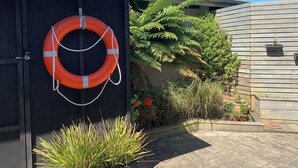 A building with a black door, a lifebuoy hanging on the door, and a garden with ferns and potted plants.