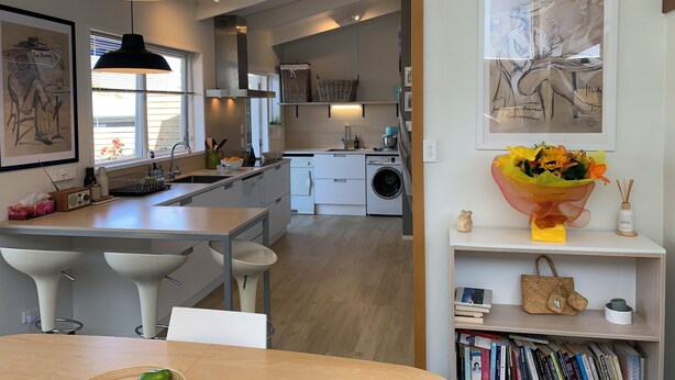 A modern kitchen with a central island, bar stools, a dining table, and a view into the dining area.