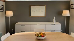 A modern dining area with a round table, a bowl of fruit, a white console table, and two floor lamps.