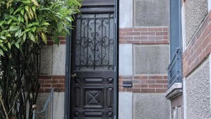 Uma porta de madeira escura com detalhada ferragem, parede de tijolos e um pequeno vaso de planta.