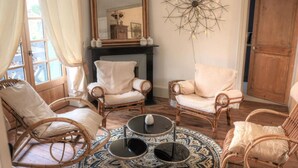 Uma sala de estar acolhedora com cadeiras de vime, um tapete estampado, uma lareira e um objeto decorativo na parede.