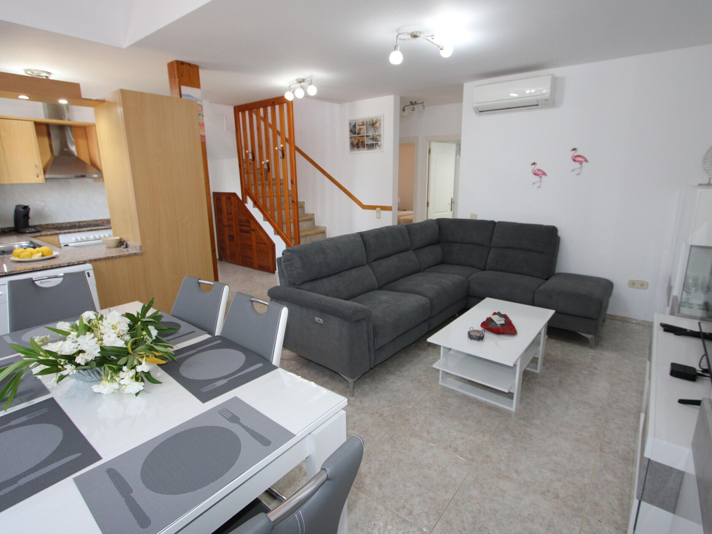 A modern living room with a grey sectional sofa, a dining table with chairs, a white coffee table, and a kitchen area with a stove and sink.