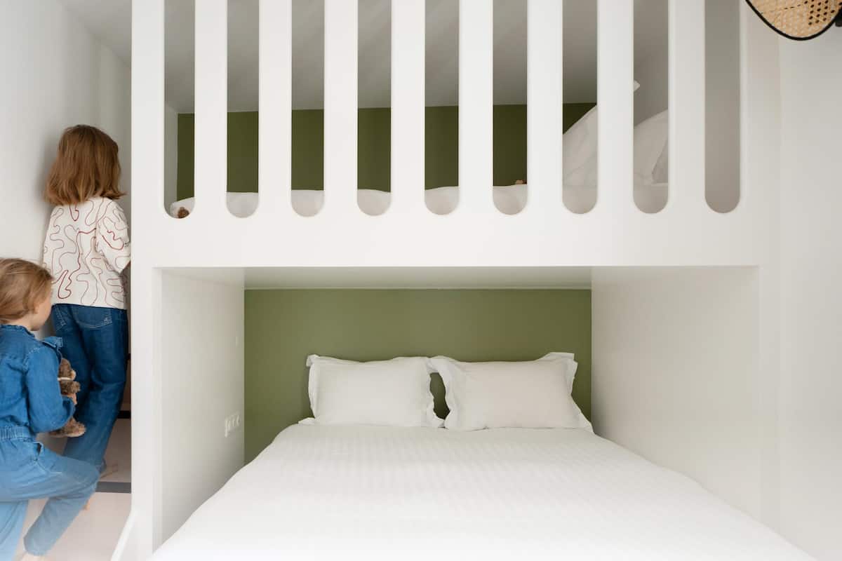 A bunk bed with a white headboard and green wall behind it.