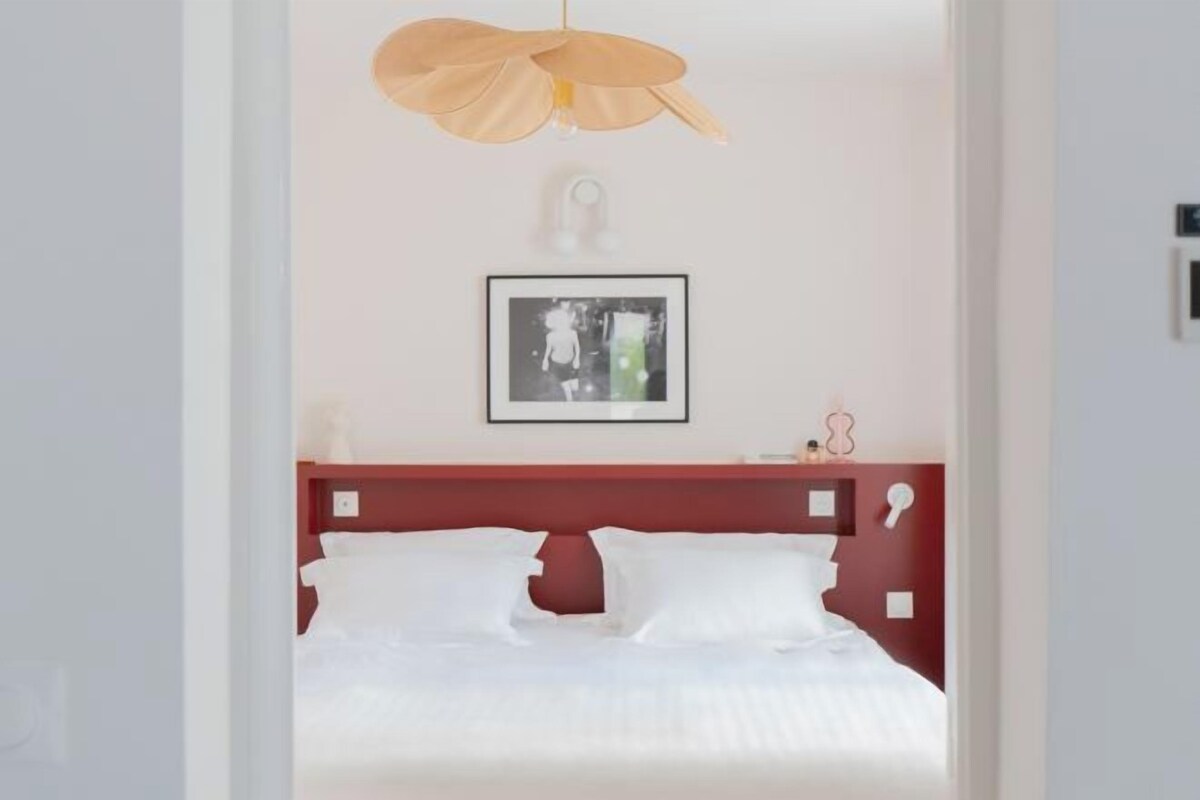 A hotel room with a bed, a red headboard, a framed picture on the wall, and a pendant light.