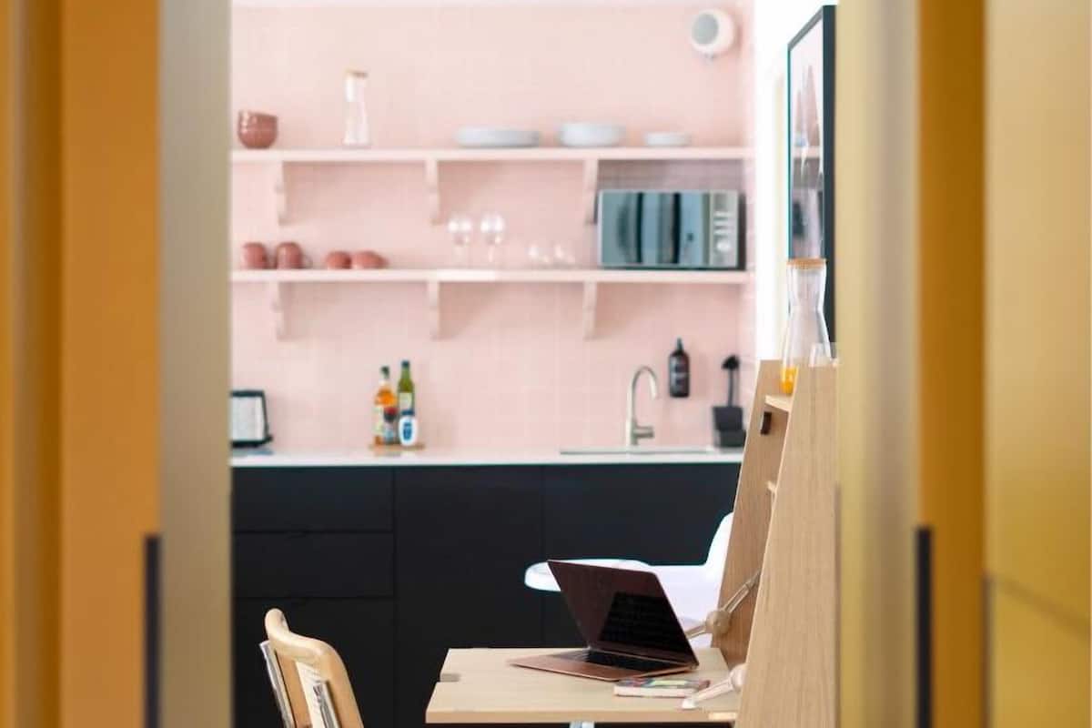 A modern kitchen with a laptop on a wooden stand, a chair, and a sink.