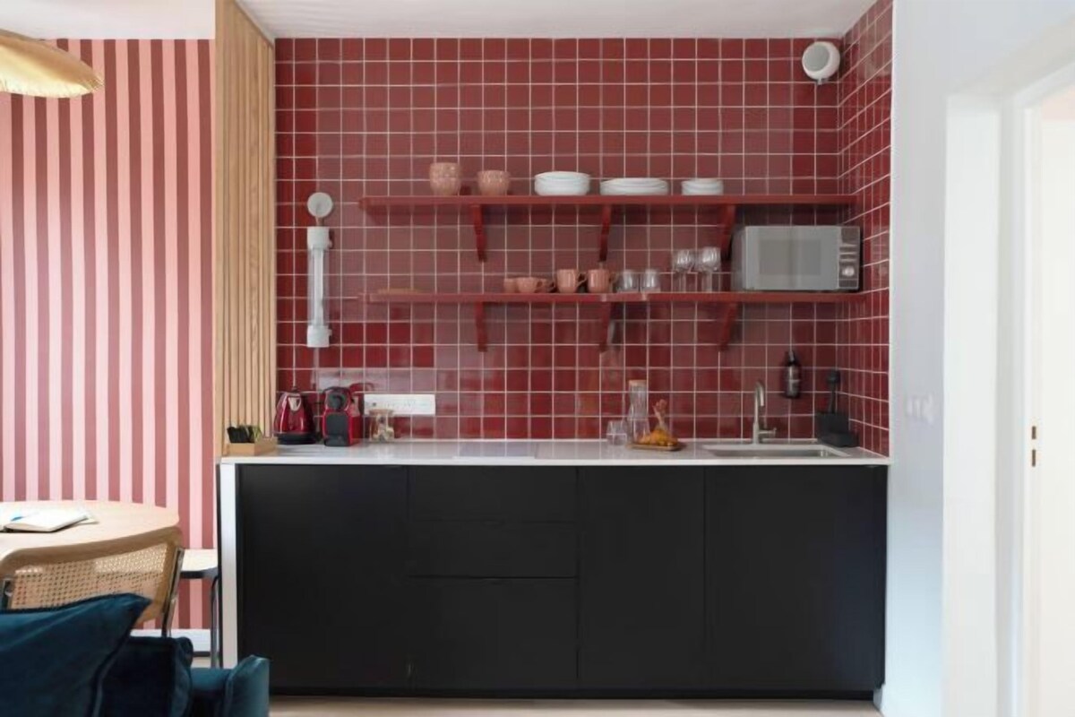 A kitchen with red tiled backsplash, black cabinets, and a white countertop.