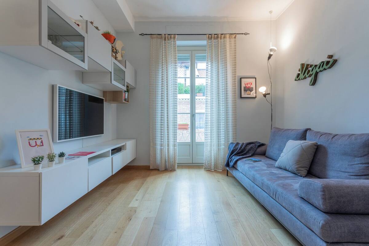 Una sala de estar moderna con un sofá gris, un televisor de pantalla plana y un mueble de entretenimiento blanco.