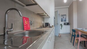 A modern kitchen with a stainless steel sink, a red informational sign, a dining area with a table and chairs, and a kitchen island. - La Casa dei Viaggiatori by Wonderful Italy (Turin)