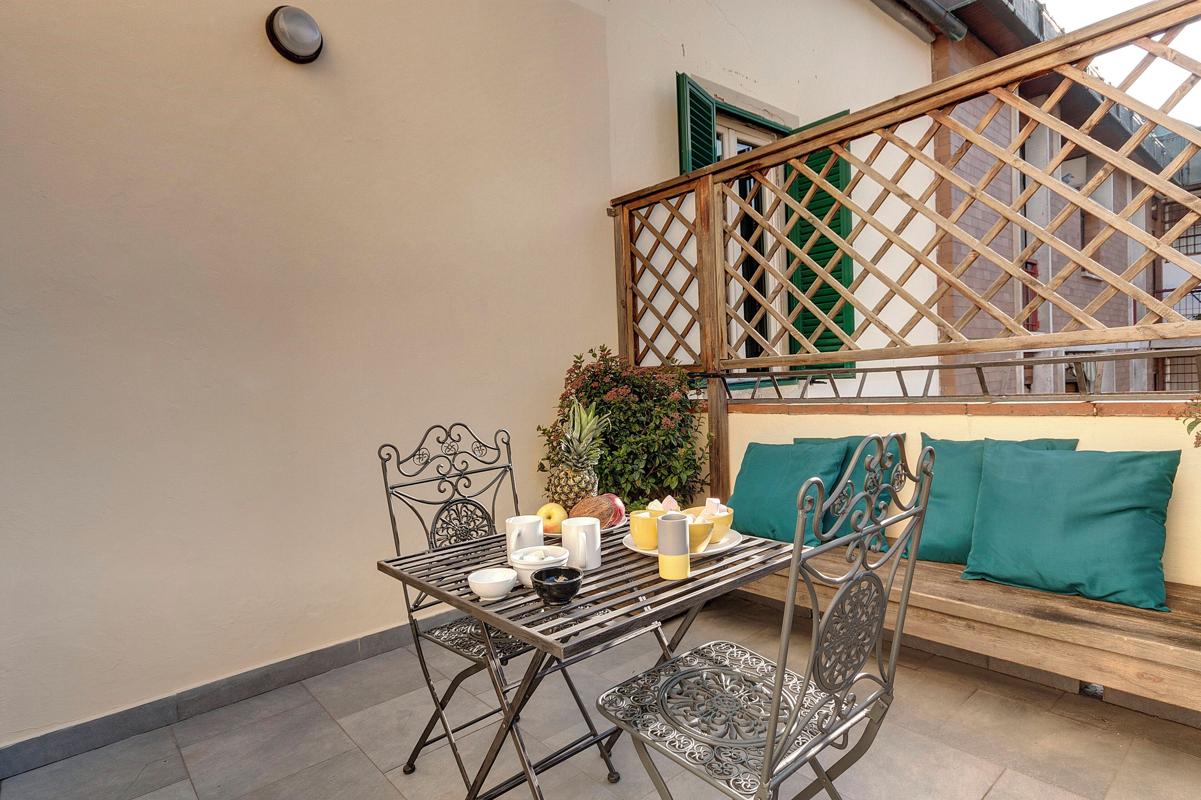 A metal table with chairs, a wooden bench with green cushions, and a wooden lattice partition.