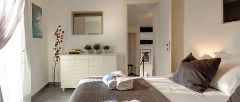 A hotel room with a bed, a dresser, a mirror, and an air conditioning unit.