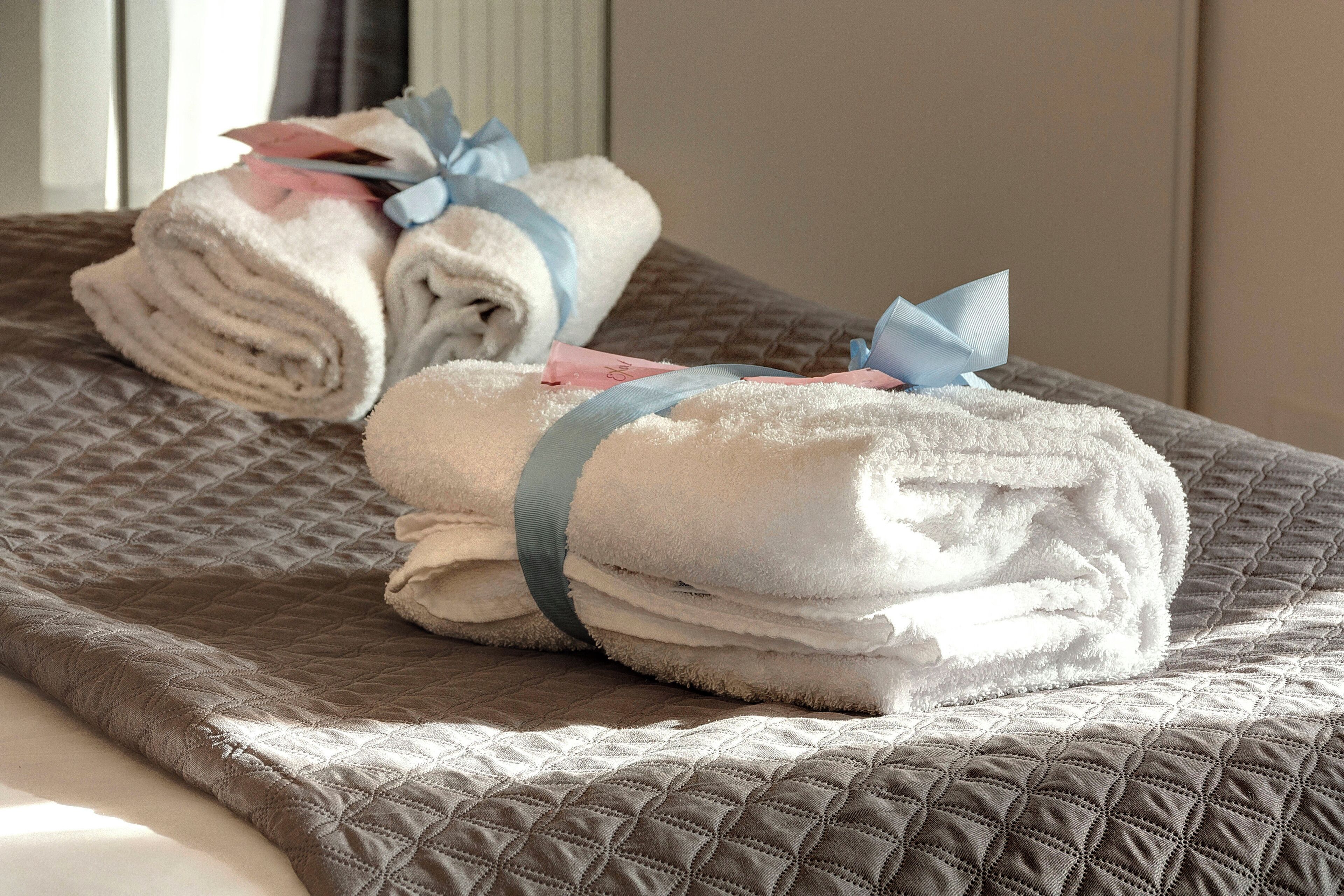 Een net opgemaakt bed met opgevouwen handdoeken en een blauw lint.