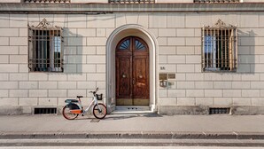 En byggnad med en stor trädörr, två fönster med metallgaller och en cykel parkerad framför.