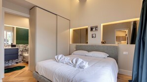 Una habitación de hotel moderna con una cama grande, un baño con pared de mármol y un espejo sobre la cama.