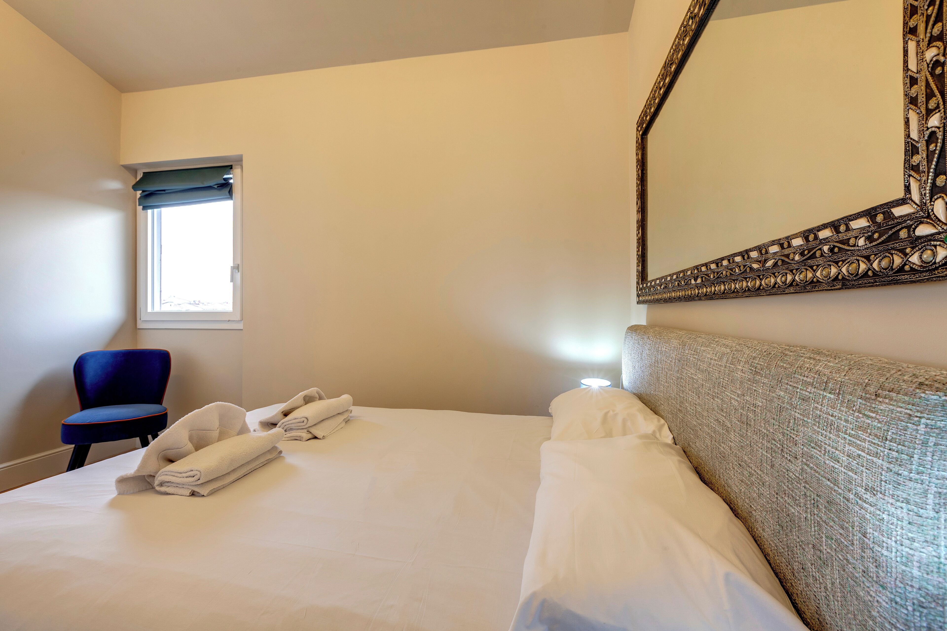 A hotel room with a neatly made bed, a chair, a window with a view, and a large mirror.