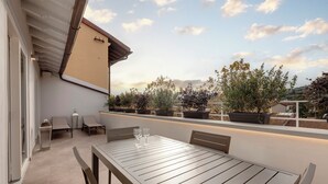 Un patio exterior con mesa y sillas de madera, plantas en macetas y una pérgola.