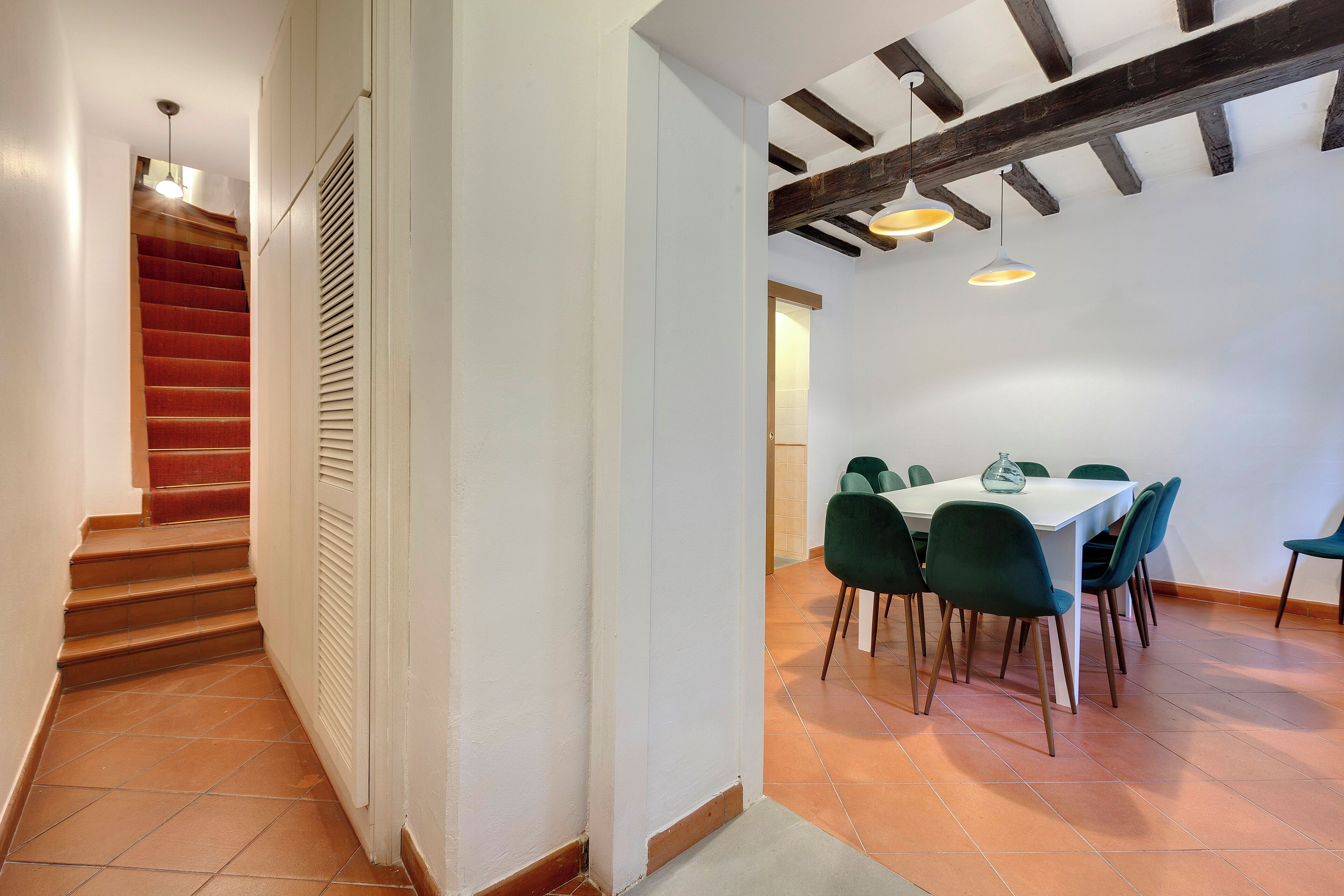 A staircase leading to a dining area with a white table and green chairs.