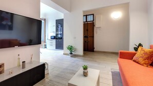 Un salon moderne avec un téléviseur à écran plat, une table basse et un canapé. On aperçoit une porte en bois et une plante en pot à l’arrière-plan.