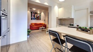 Une cuisine moderne dotée d’un îlot central, de meubles blancs et d’un canapé rouge dans l’espace de vie adjacent.