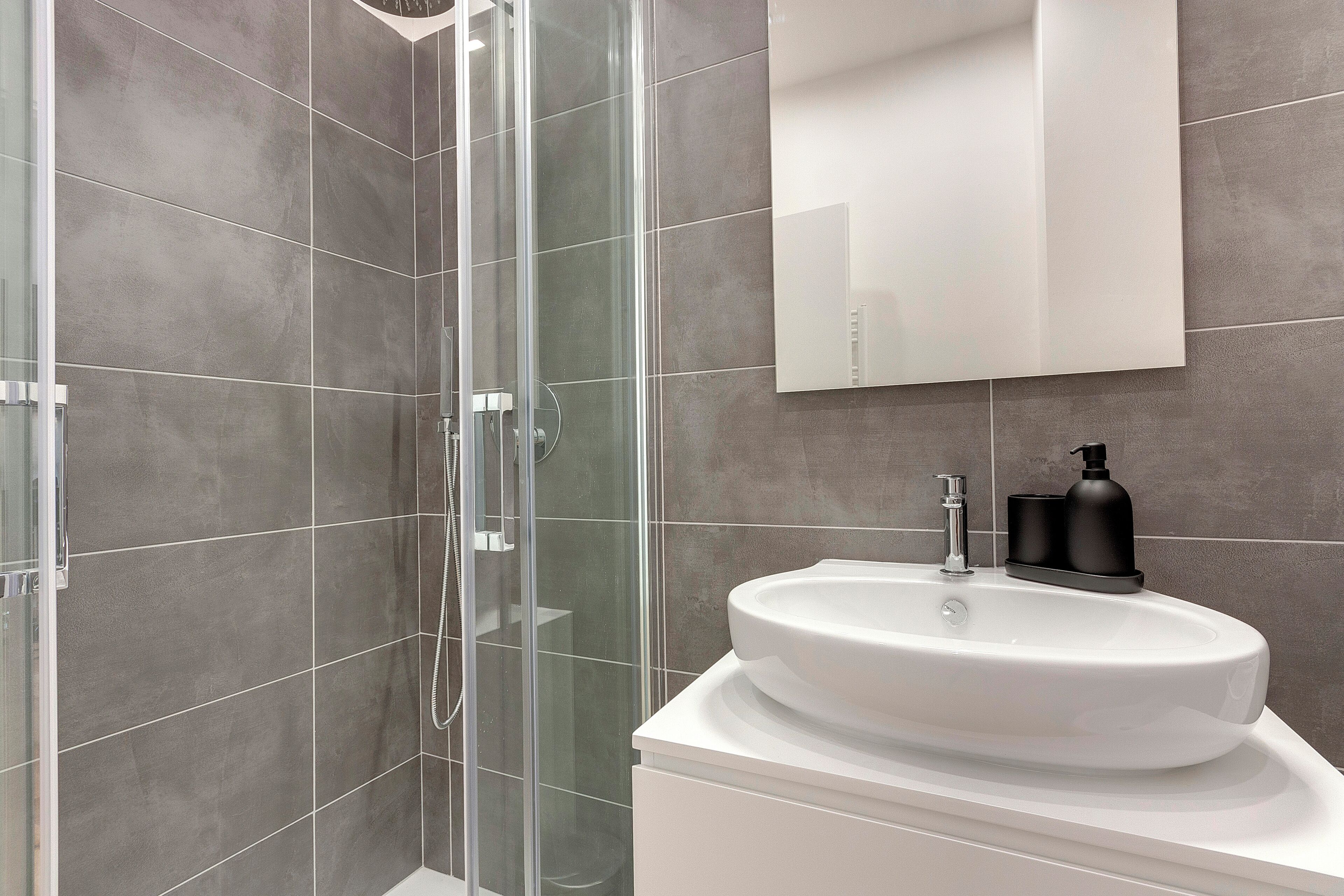 Ein modernes Badezimmer mit einer Glaskabine zur Dusche, einem weißen Waschbecken und einem großen Spiegel.