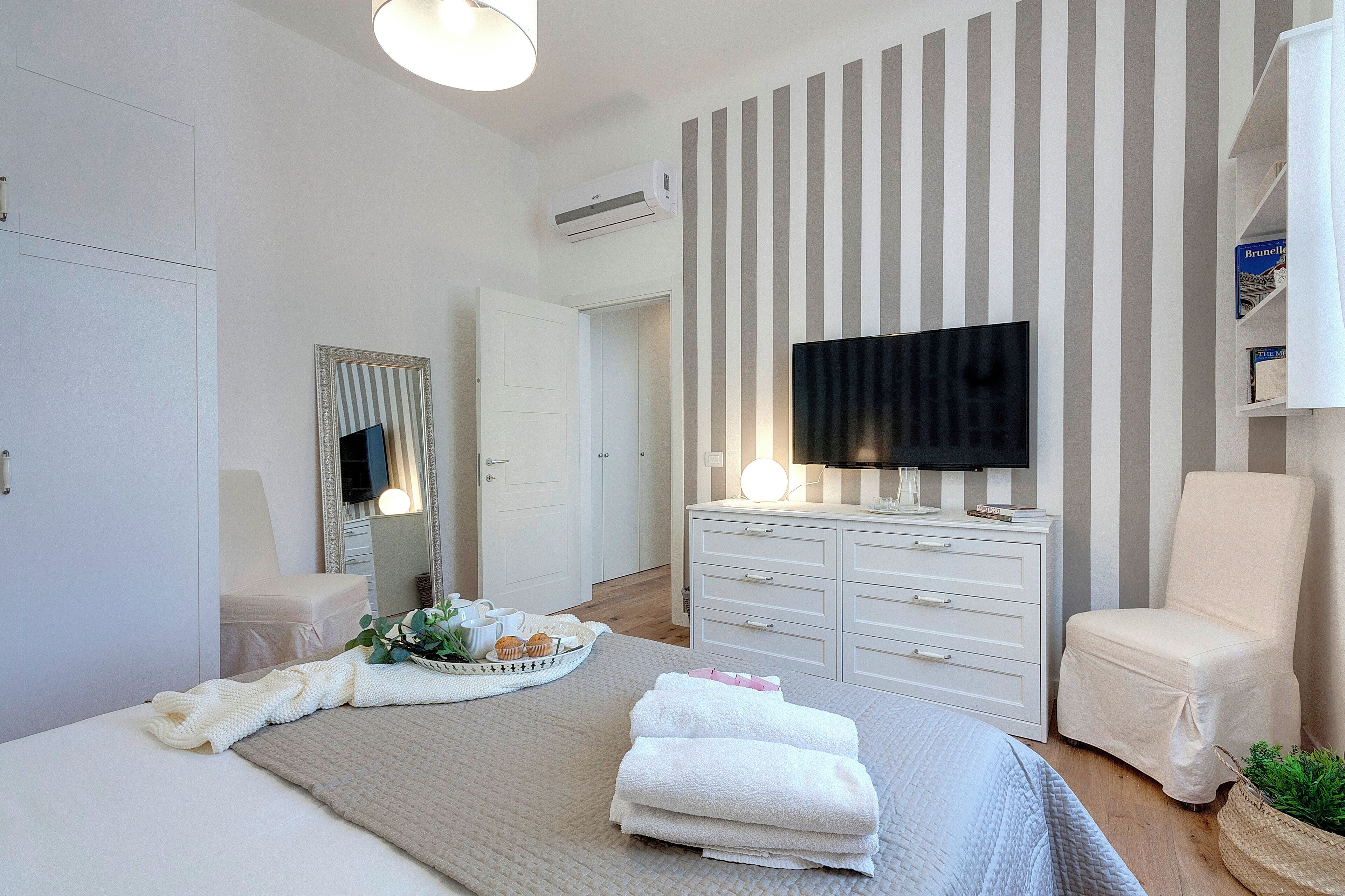 A modern bedroom with a bed, a TV, a dresser, and a chair.