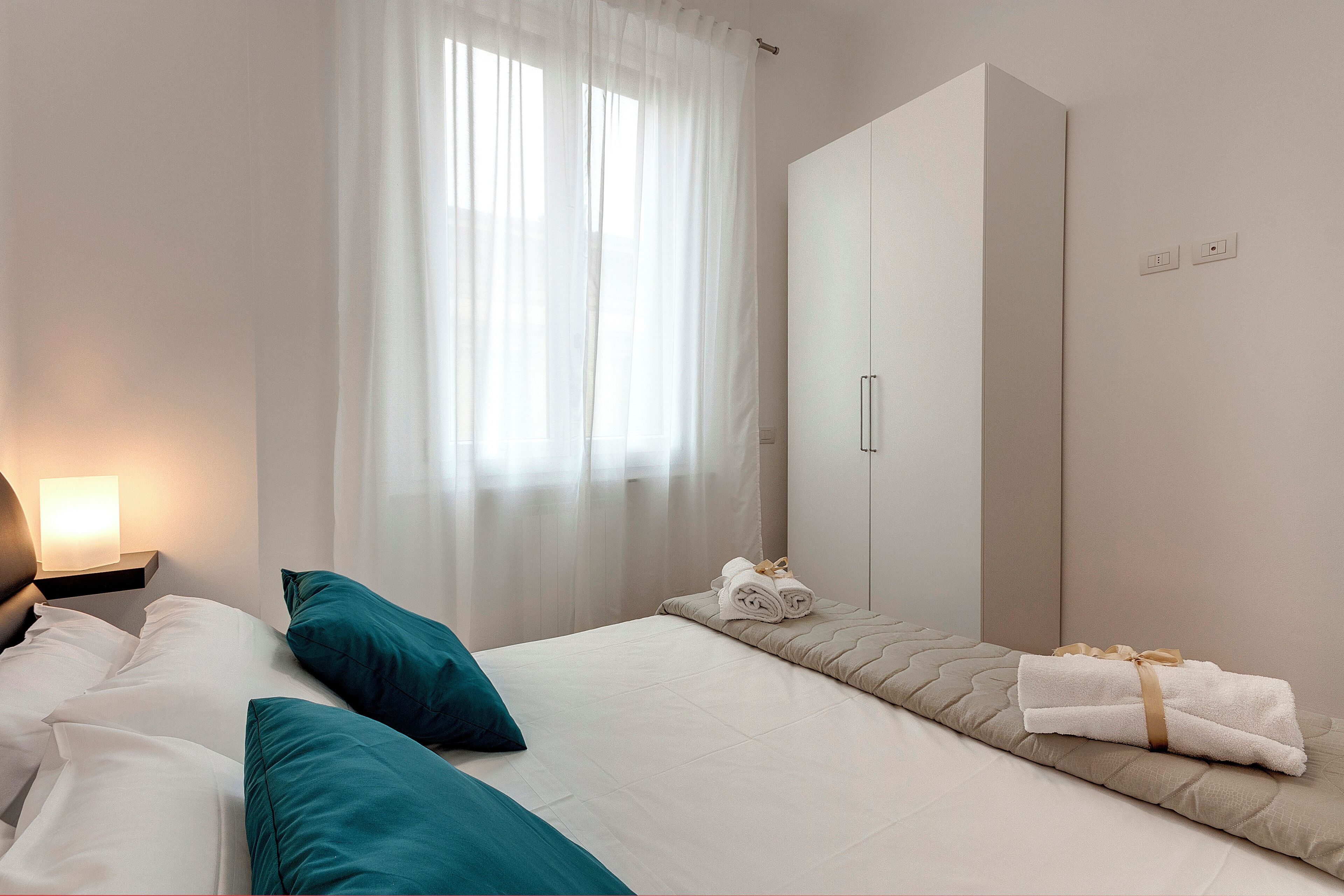 Une chambre d’hôtel avec un lit, une table de chevet, une armoire et une fenêtre avec des rideaux.