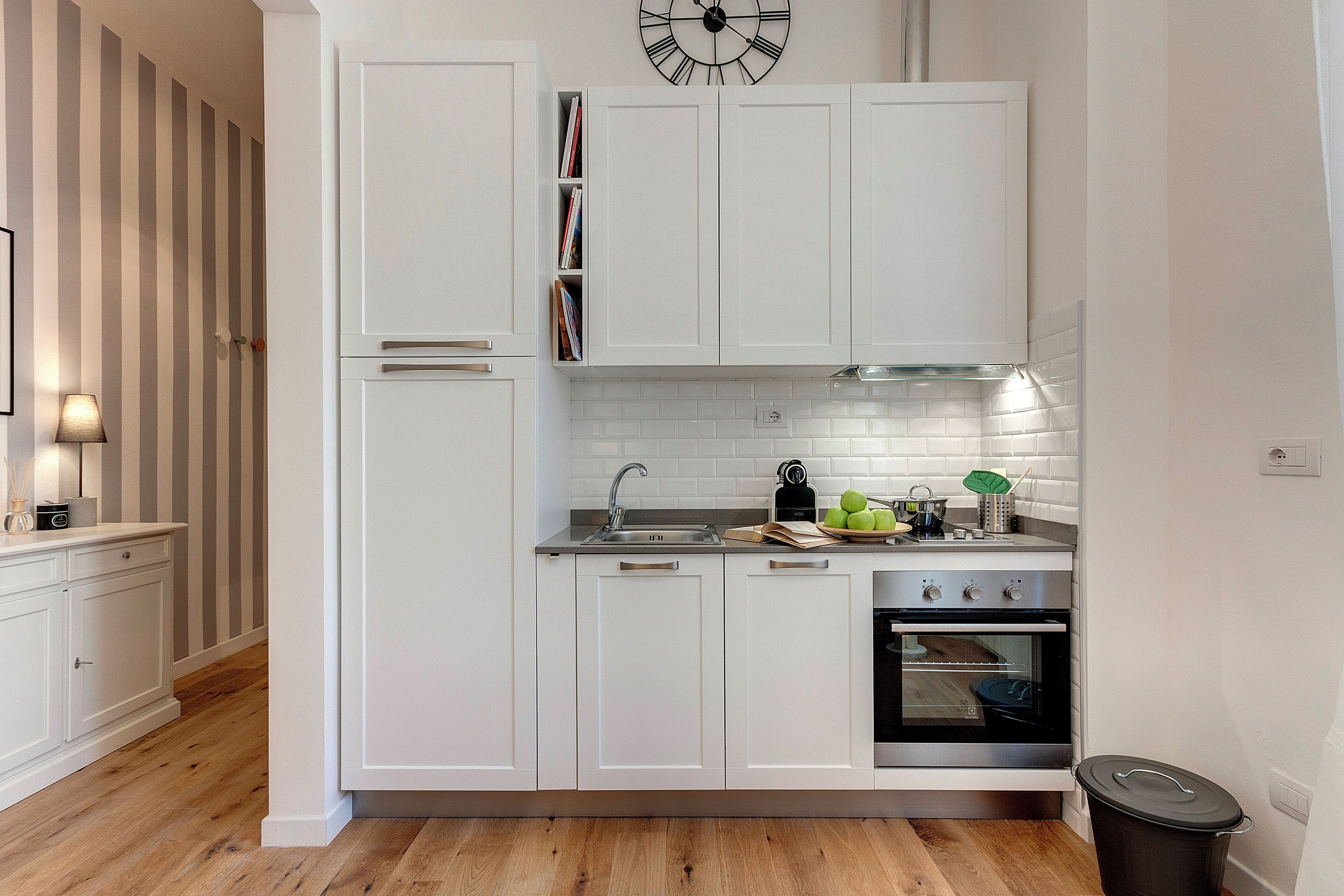 A modern kitchen with white cabinetry, a stainless steel sink, a clock, and a stove.