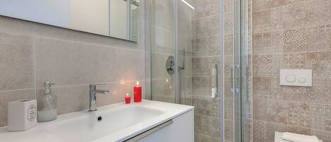 Un baño moderno con ducha envuelta en vidrio, un lavabo blanco con espejo arriba y baldosas estampadas en las paredes.