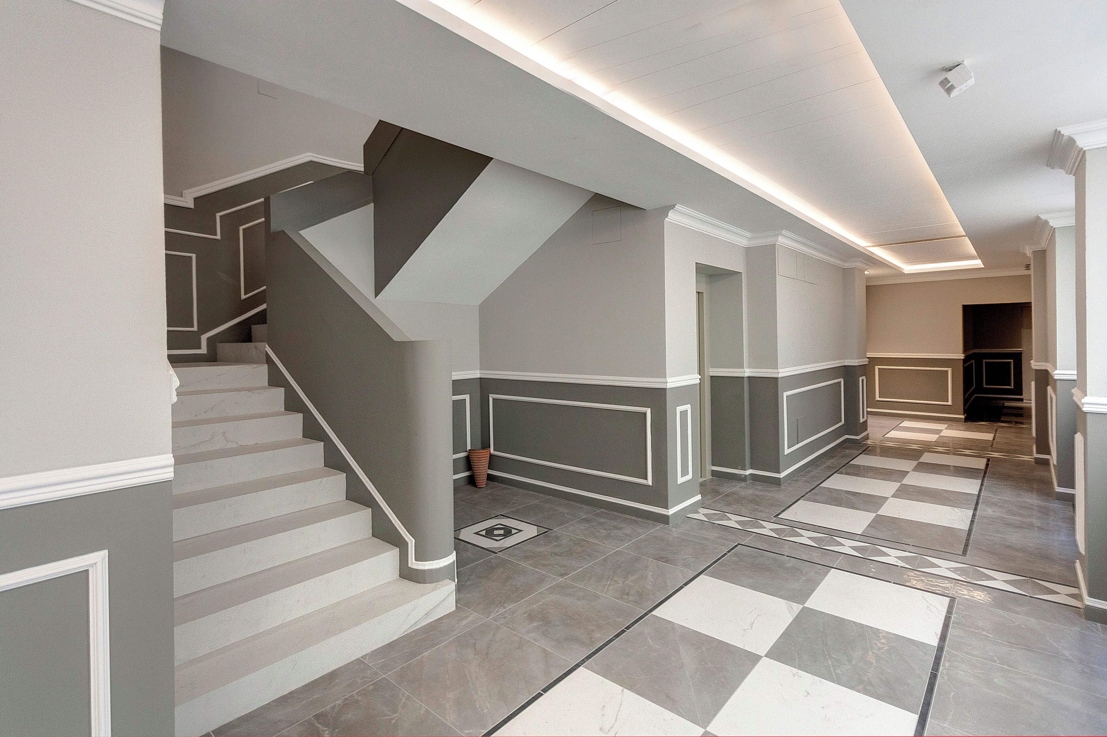 A modern interior with a staircase, checkered floor tiles, and recessed lighting.