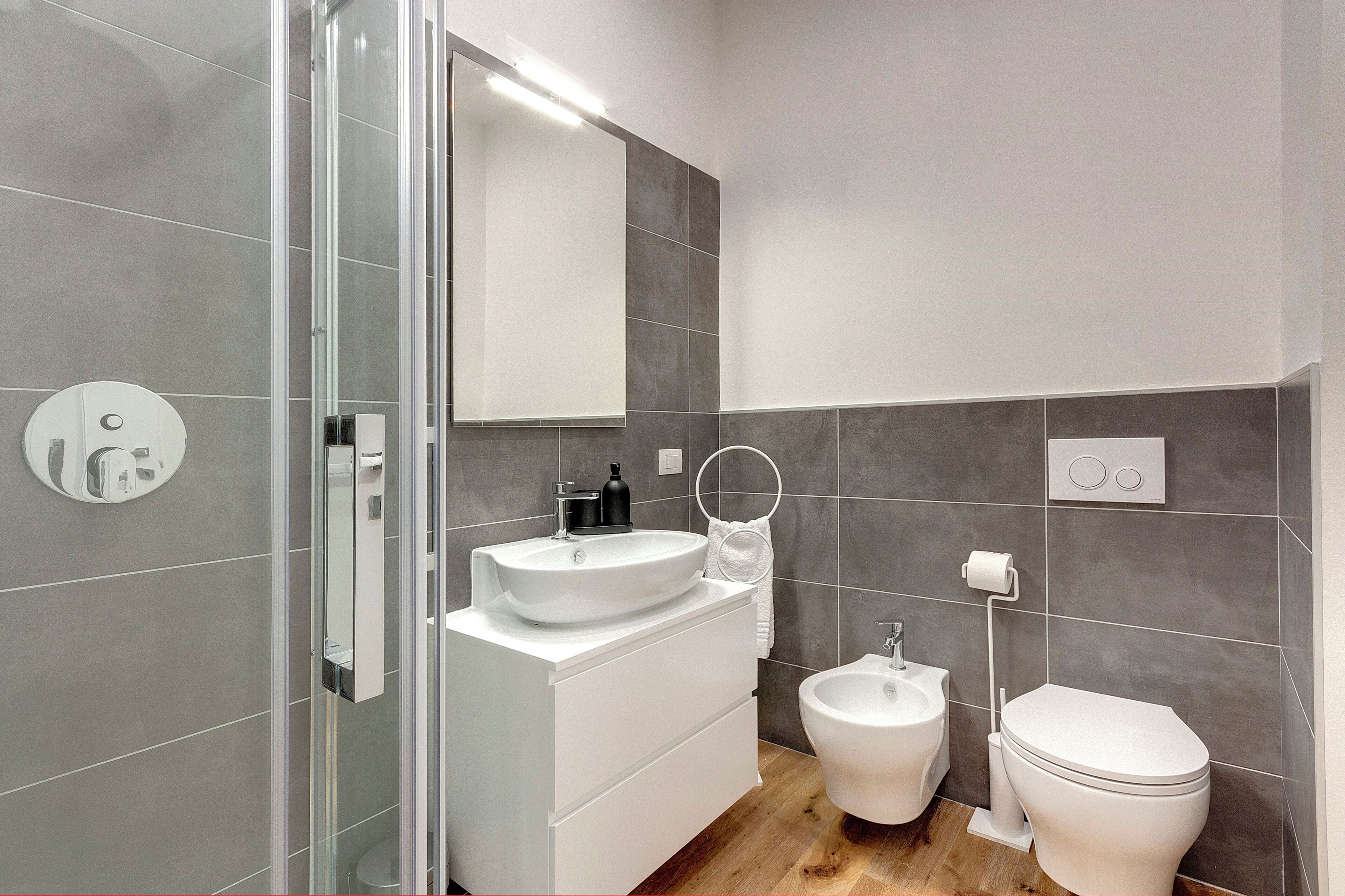 A modern bathroom with a glass shower enclosure, a white sink, a bidet, and a toilet.