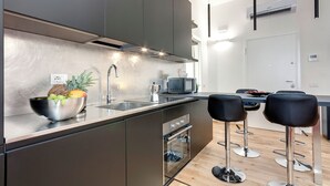 A modern kitchen with stainless steel appliances, a built-in oven, and a bar area with stools. - Mamo Florence - Cavour Apartments (Florence)