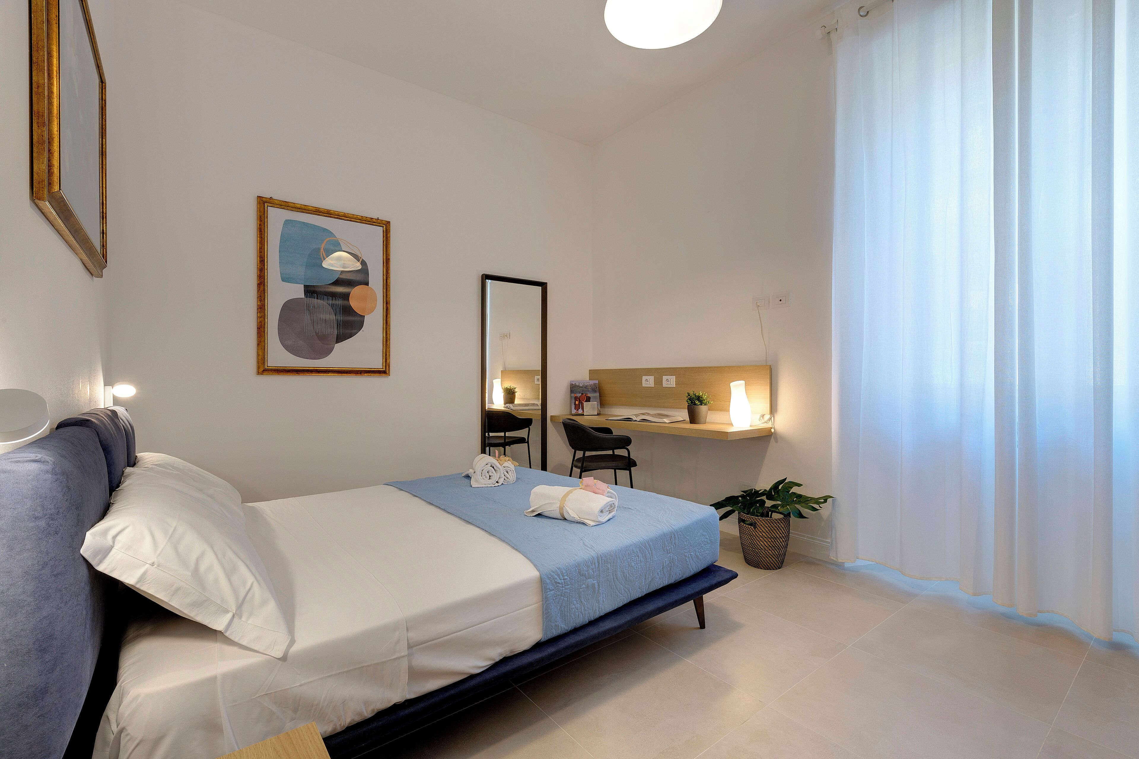 Una habitación de hotel moderna con cama, mesita de noche, escritorio, silla y una planta en maceta.