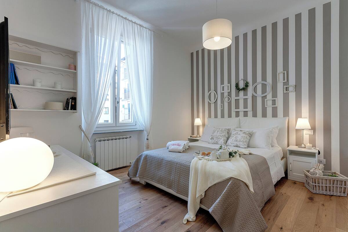 A bedroom with a bed, bedside tables, a lamp, a window with curtains, and a radiator.