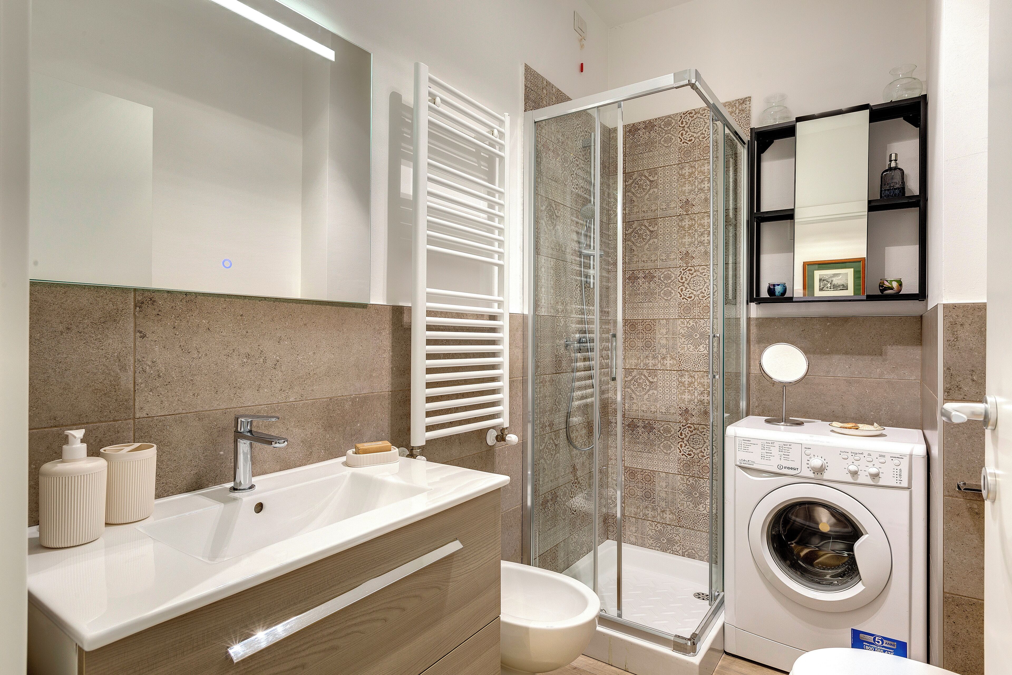 Une salle de bain moderne dotée d’un double lavabo, d’une cabine de douche en verre et d’un lave-linge encastré.