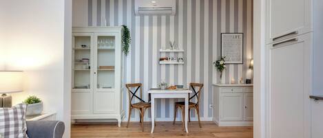 A dining area with a white table and chairs, a striped wall, and a white cabinet with glass doors.