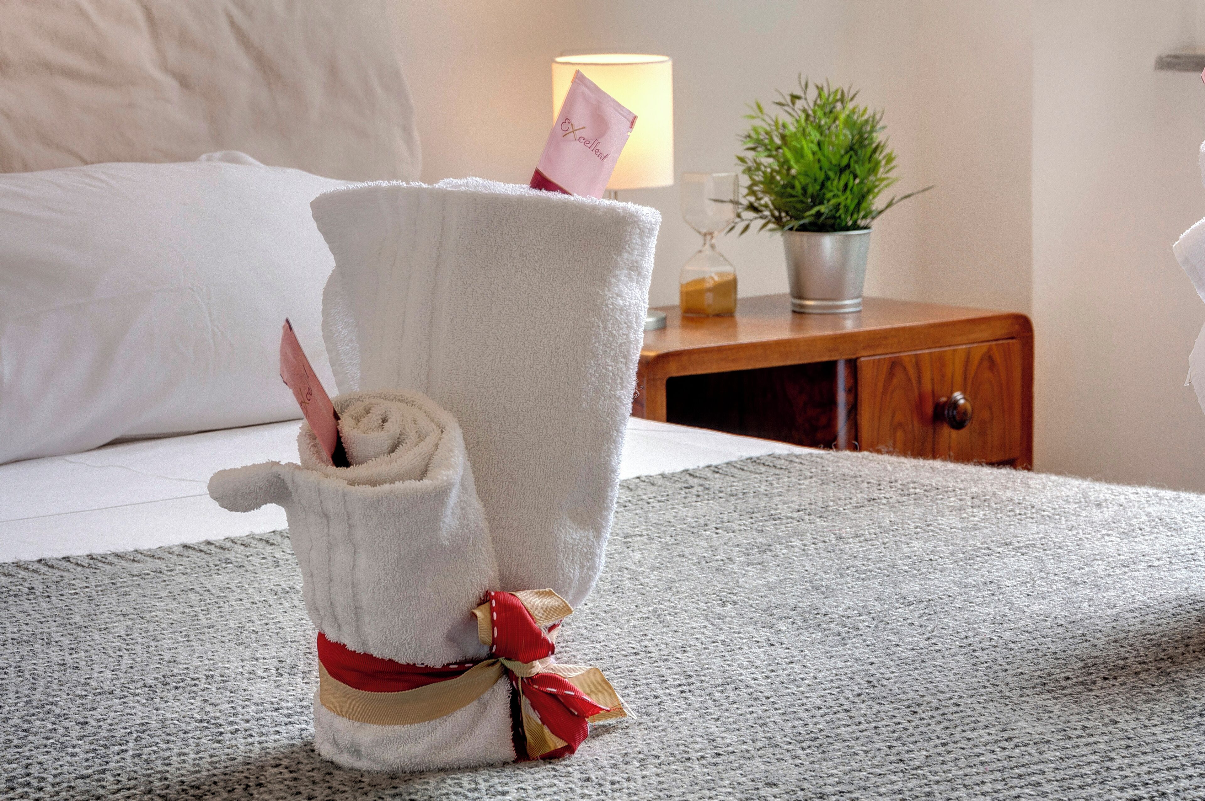 Una toalla bien doblada con un lazo, sobre una alfombra texturizada en una habitación de hotel.