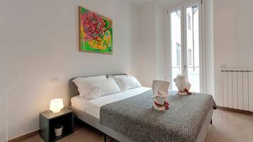 A bedroom with a bed, bedside table, lamp, radiator, and a window with blinds.
