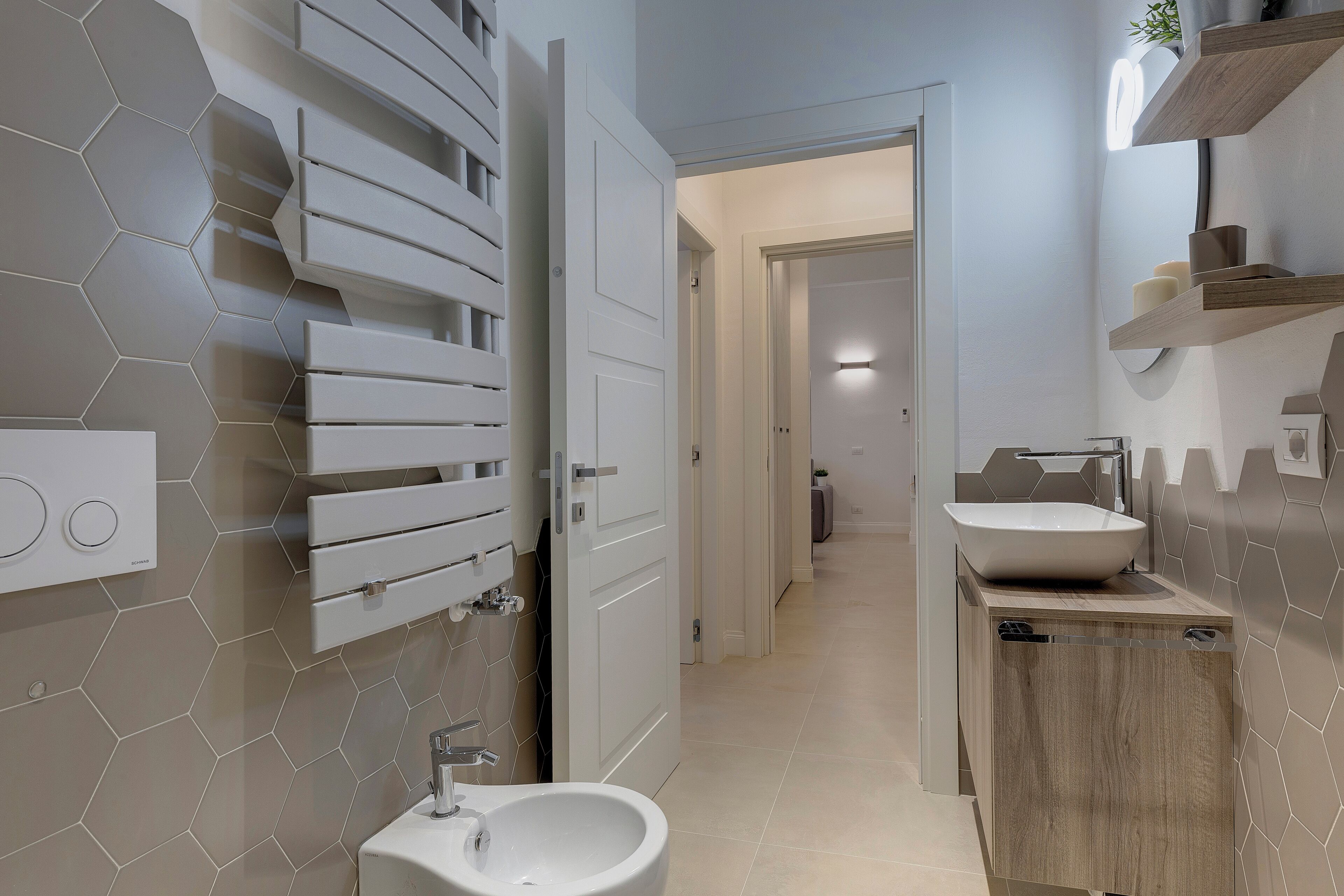 A modern bathroom with a hexagonal tile backsplash, a white sink, and a wooden vanity.