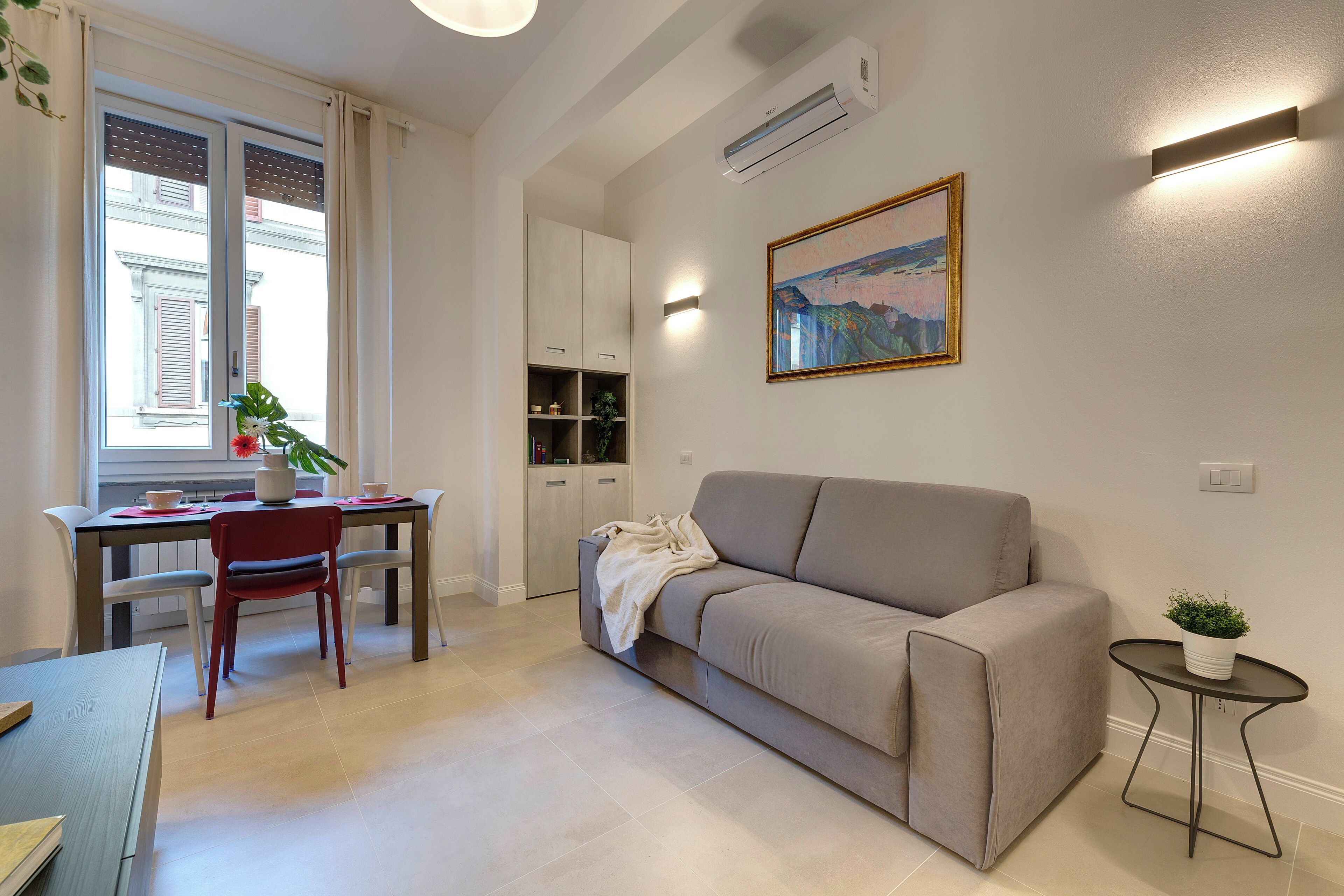 En moderne stue med sofa, spisebord og stole. Der står en potteplante på bordet, og der hænger et billede på væggen.