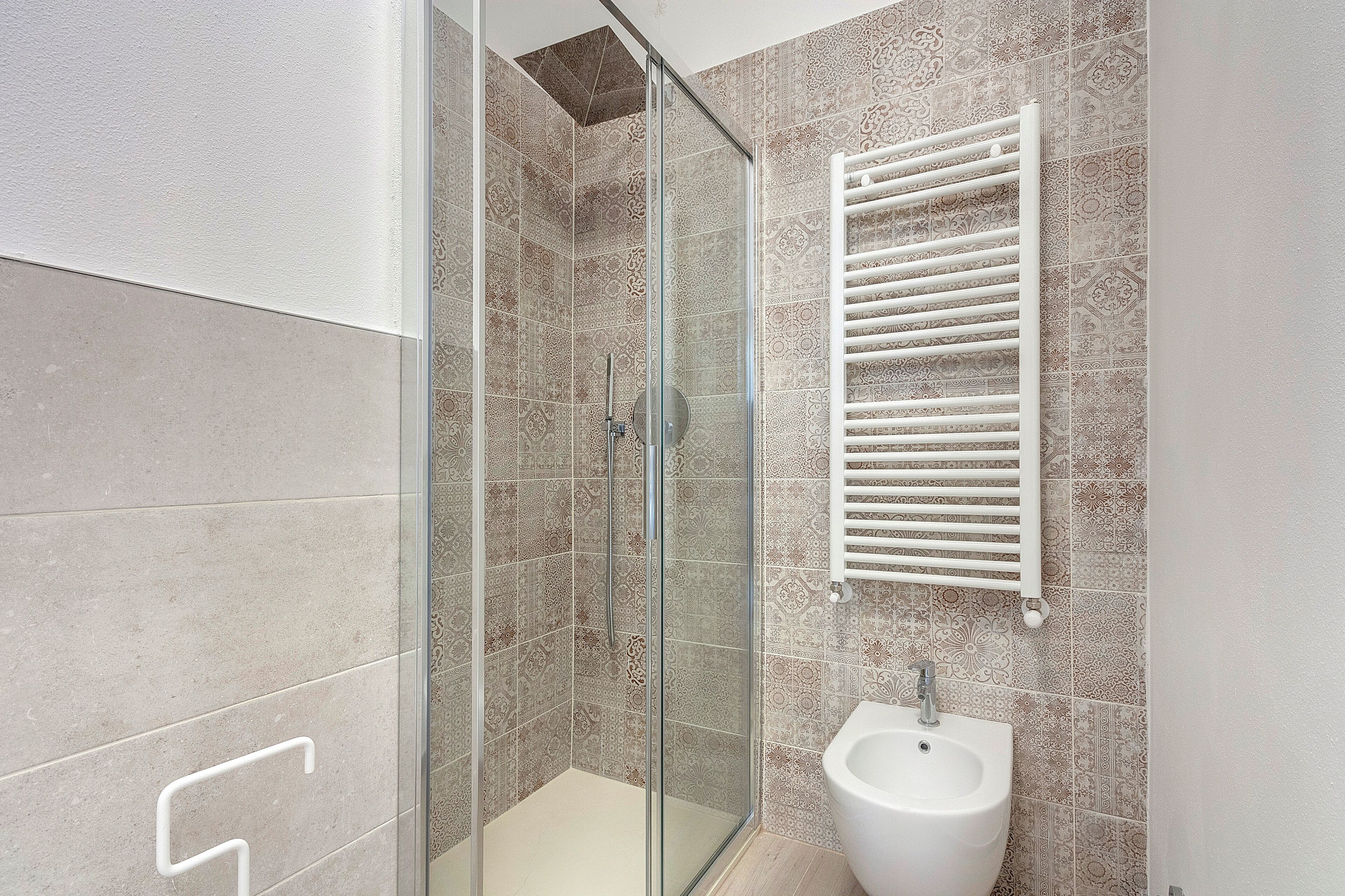 A modern bathroom with a glass-enclosed shower, a bidet, and patterned tiles.