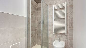 A modern bathroom with a glass-enclosed shower, a bidet, and patterned tiles.