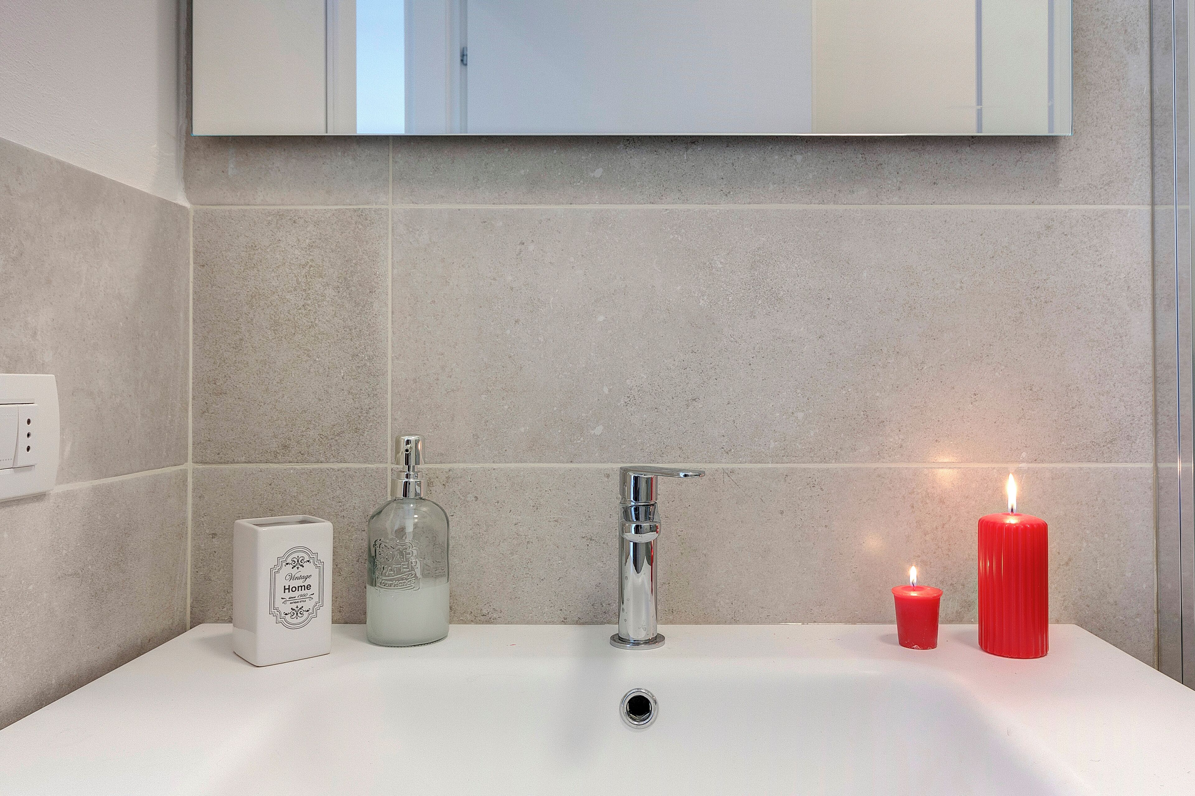 A bathroom with a white sink, a chrome faucet, a glass soap dispenser, and two red candles.