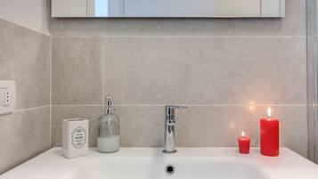 Un baño con un lavabo blanco, un grifo cromado, un dispensador de jabón de vidrio y dos velas rojas.